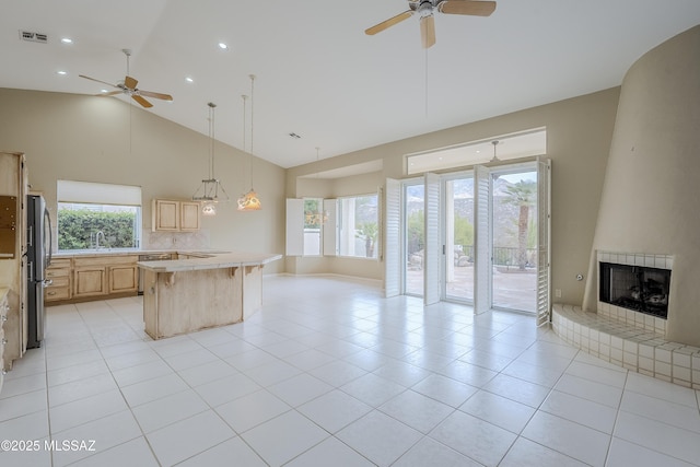 kitchen featuring light brown cabinets, open floor plan, ceiling fan, a large fireplace, and light countertops