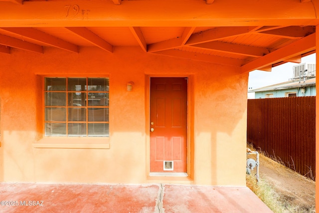 view of exterior entry featuring stucco siding and fence