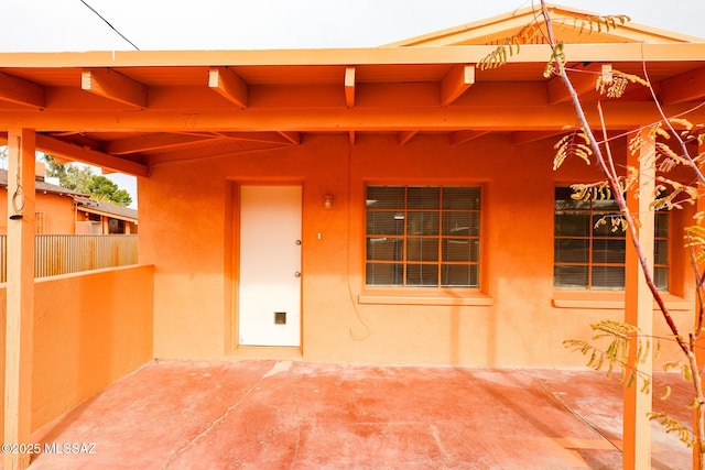 entrance to property featuring a patio area, fence, and stucco siding