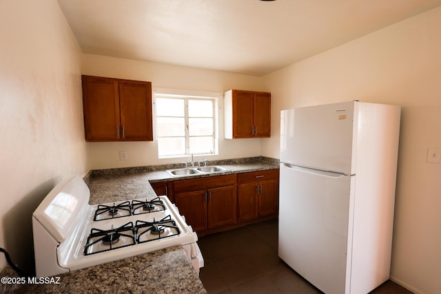kitchen with brown cabinetry, white appliances, dark tile patterned flooring, and a sink