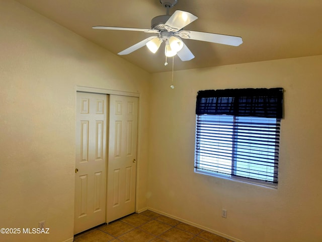 unfurnished bedroom featuring a closet, baseboards, tile patterned flooring, lofted ceiling, and ceiling fan