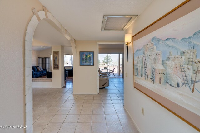 corridor featuring baseboards, arched walkways, and tile patterned flooring
