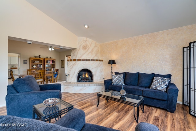 living area featuring a high end fireplace, baseboards, wood finished floors, high vaulted ceiling, and a ceiling fan