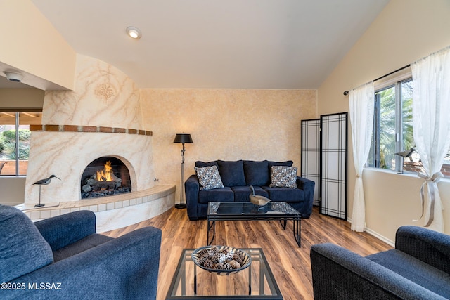 living room with vaulted ceiling, wood finished floors, and a warm lit fireplace
