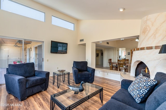 living room featuring visible vents, a premium fireplace, wood finished floors, high vaulted ceiling, and a ceiling fan