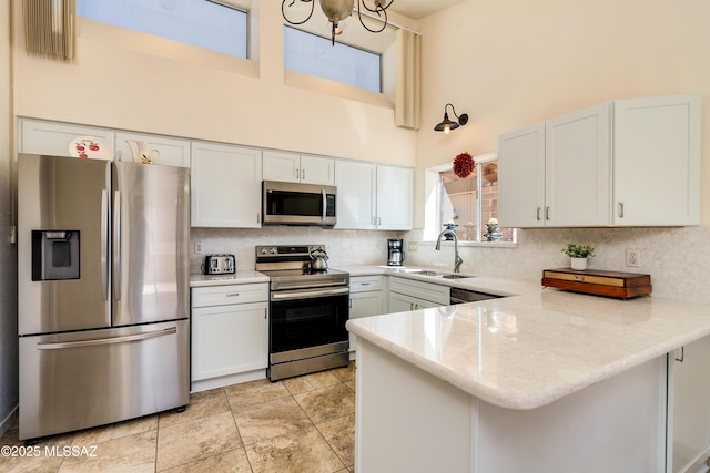 kitchen featuring a sink, tasteful backsplash, stainless steel appliances, a peninsula, and a towering ceiling