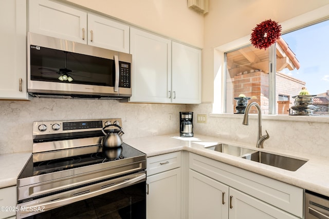 kitchen featuring backsplash, white cabinets, stainless steel appliances, and a sink