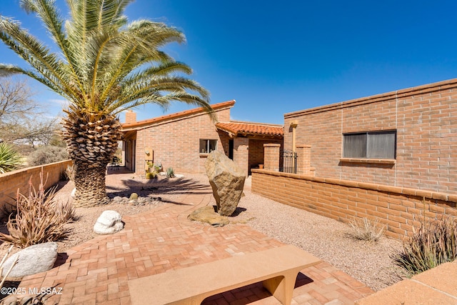 view of front of home with a patio, brick siding, and fence