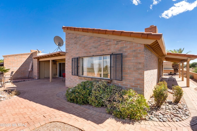 rear view of property with a patio, brick siding, and a chimney