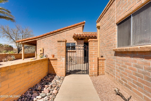 view of side of property with a tiled roof, a gate, fence, and brick siding