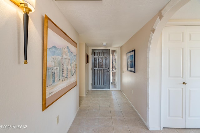 hall featuring baseboards, arched walkways, a textured ceiling, and light tile patterned flooring