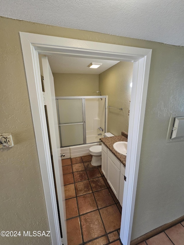 bathroom with vanity, toilet, a textured wall, and combined bath / shower with glass door