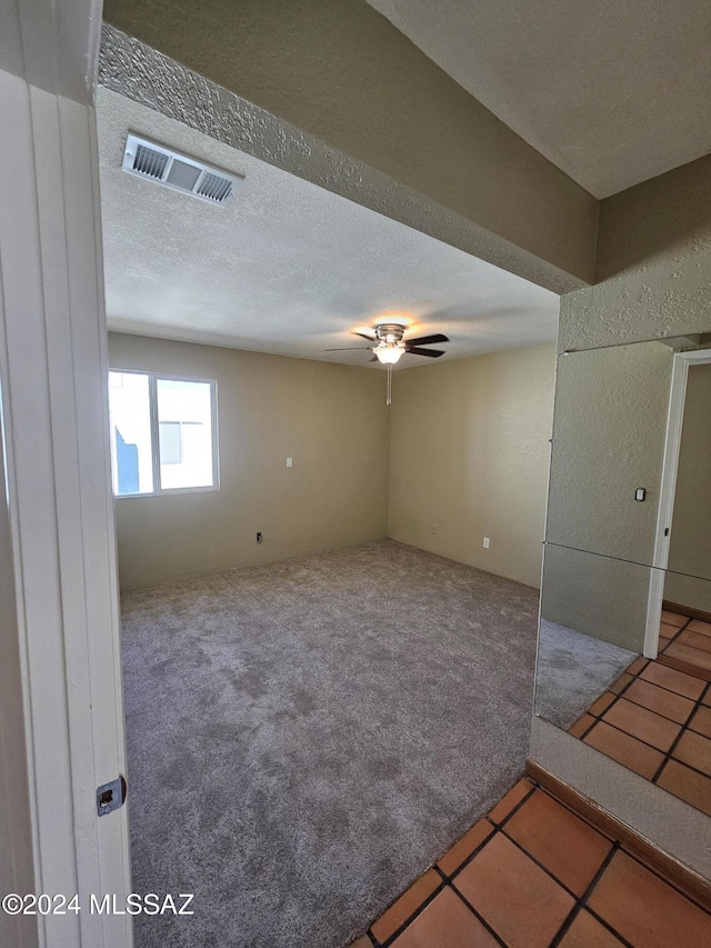 tiled spare room featuring carpet flooring, a ceiling fan, visible vents, and a textured ceiling