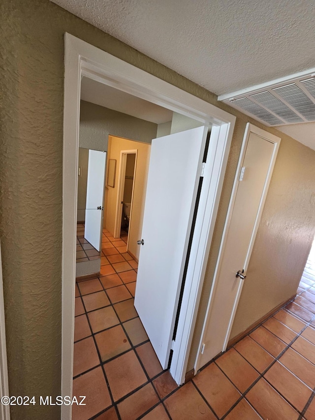 corridor with visible vents, a textured ceiling, light tile patterned flooring, and a textured wall