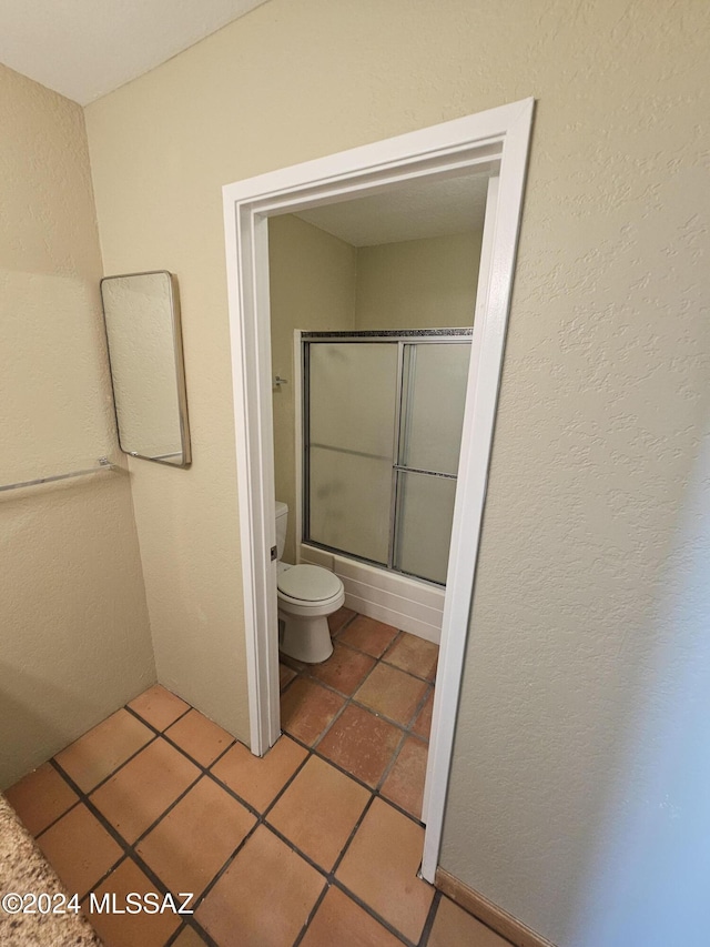 full bath featuring tile patterned floors, toilet, a textured wall, and shower / bath combination with glass door