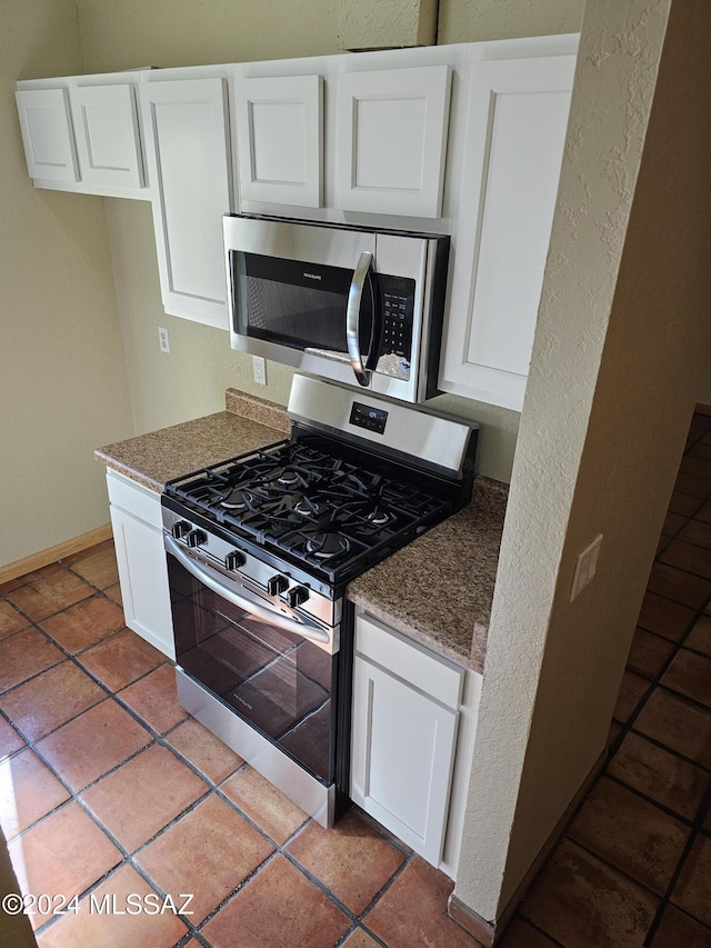kitchen with baseboards, dark stone countertops, appliances with stainless steel finishes, a textured wall, and white cabinets