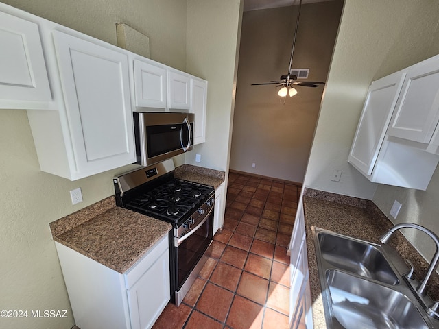 kitchen with dark countertops, appliances with stainless steel finishes, white cabinets, a ceiling fan, and a sink
