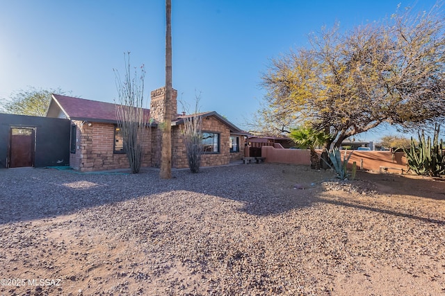 rear view of property with stone siding, a chimney, and fence