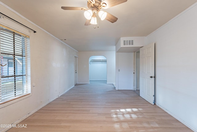 hallway featuring crown molding, light wood-style flooring, arched walkways, and visible vents