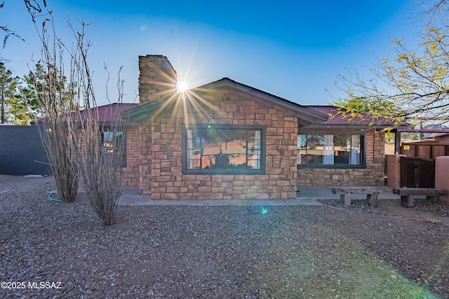 view of side of property featuring stone siding, fence, and a shingled roof