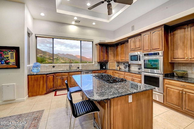 kitchen featuring a tray ceiling, dark stone countertops, appliances with stainless steel finishes, light tile patterned flooring, and a sink