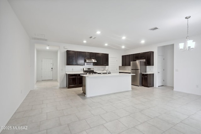 kitchen featuring light countertops, appliances with stainless steel finishes, under cabinet range hood, visible vents, and decorative backsplash