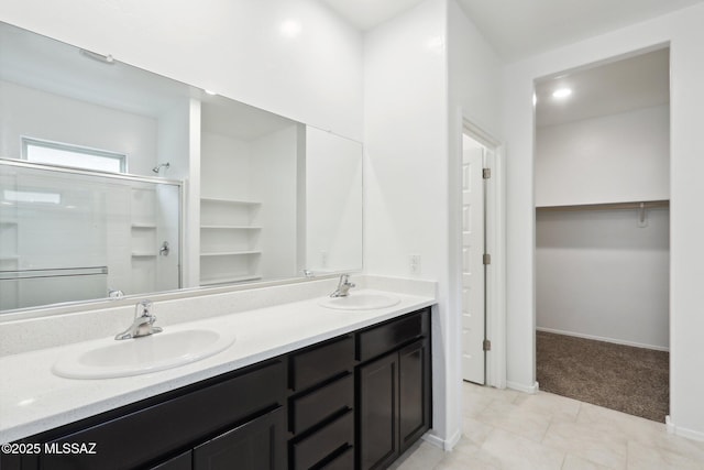 bathroom featuring a spacious closet, double vanity, a sink, and a stall shower