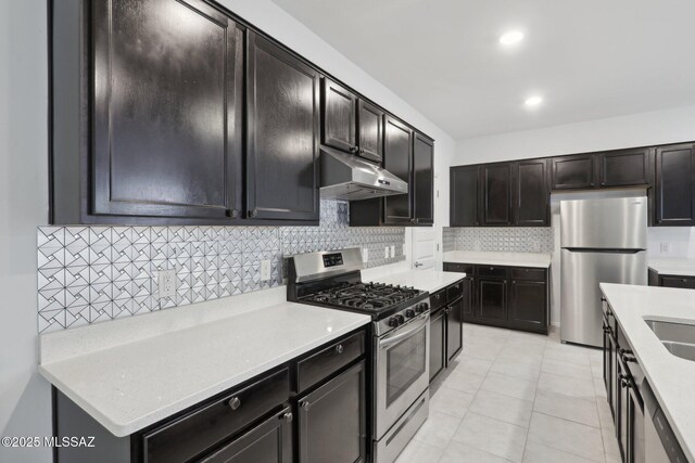 kitchen with a sink, tasteful backsplash, appliances with stainless steel finishes, under cabinet range hood, and light tile patterned floors