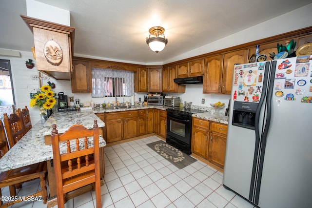 kitchen with light stone counters, black range with electric stovetop, brown cabinetry, under cabinet range hood, and fridge with ice dispenser