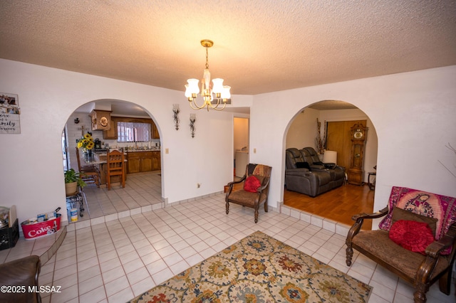 living area featuring arched walkways, a textured ceiling, tile patterned flooring, and a notable chandelier
