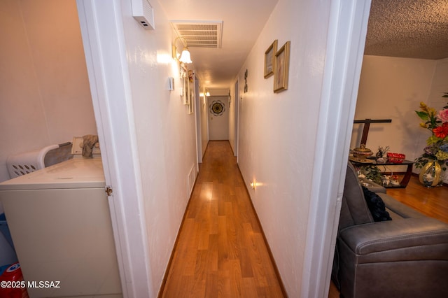 corridor with a textured ceiling, washing machine and dryer, light wood finished floors, and visible vents