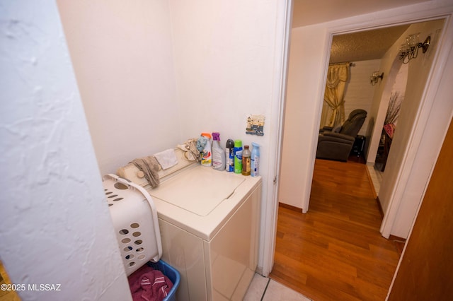 clothes washing area featuring light wood finished floors, washing machine and dryer, laundry area, and a textured ceiling