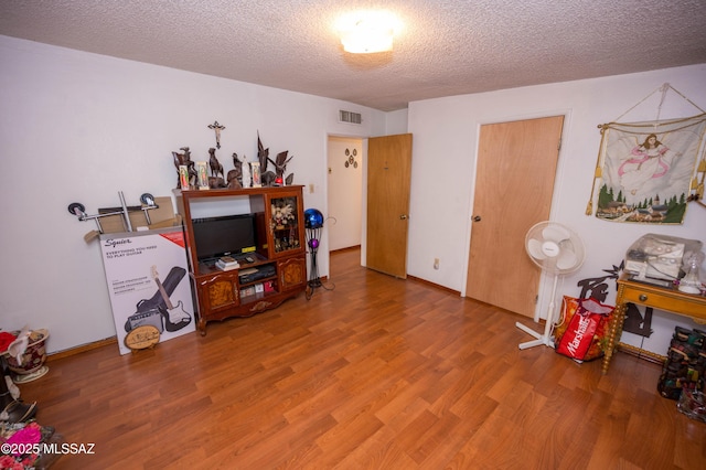 interior space with baseboards, a textured ceiling, visible vents, and wood finished floors