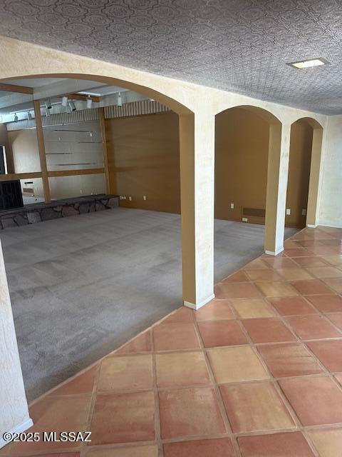 basement with arched walkways, carpet floors, and tile patterned floors