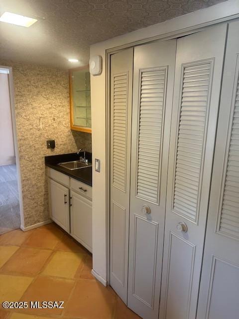kitchen featuring a sink, a textured ceiling, glass insert cabinets, light tile patterned floors, and dark countertops