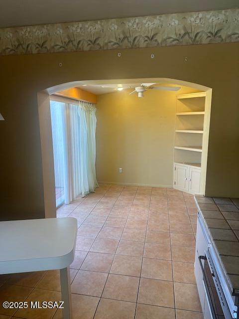 empty room with a ceiling fan, light tile patterned floors, arched walkways, and baseboards