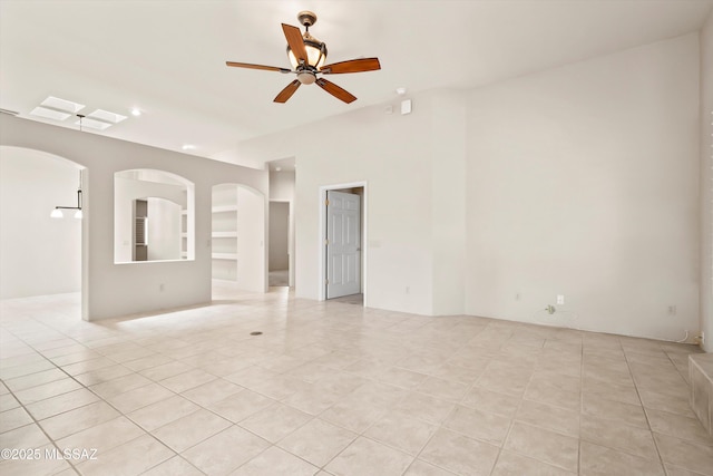 unfurnished room with arched walkways, a ceiling fan, and light tile patterned flooring