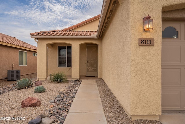 entrance to property with cooling unit, a garage, a tile roof, and stucco siding
