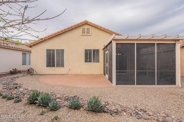 rear view of house with stucco siding, a sunroom, a patio, and a tile roof