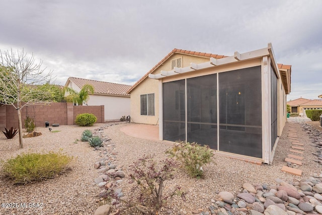 back of house featuring a tile roof, fence, a sunroom, and stucco siding
