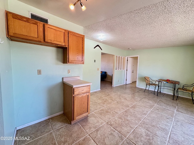kitchen with baseboards, brown cabinetry, a textured ceiling, and visible vents