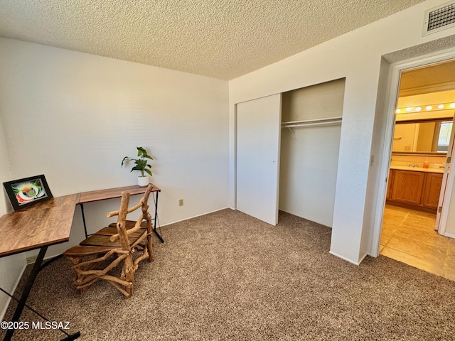 home office with a textured ceiling, visible vents, and carpet