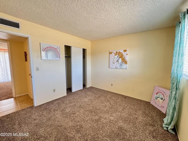 unfurnished bedroom with a textured ceiling, visible vents, carpet, and a closet