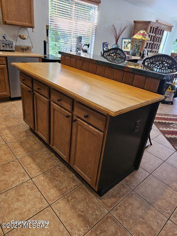 kitchen with stainless steel dishwasher, light tile patterned flooring, and wood counters