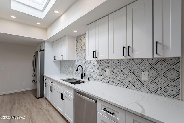 kitchen featuring a skylight, appliances with stainless steel finishes, white cabinetry, a sink, and light stone counters