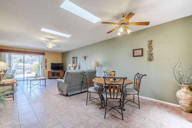 dining area featuring light tile patterned floors, lofted ceiling with skylight, baseboards, and ceiling fan