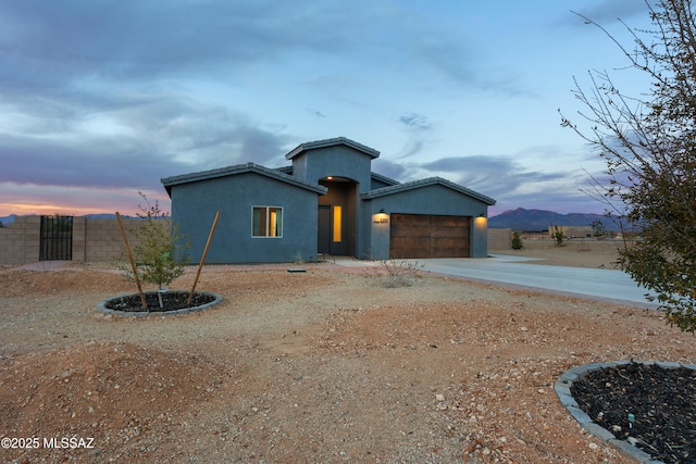 view of front facade with stucco siding, an attached garage, driveway, and fence