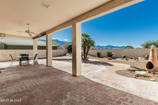 view of patio with outdoor dining area, a ceiling fan, a mountain view, and a fenced backyard