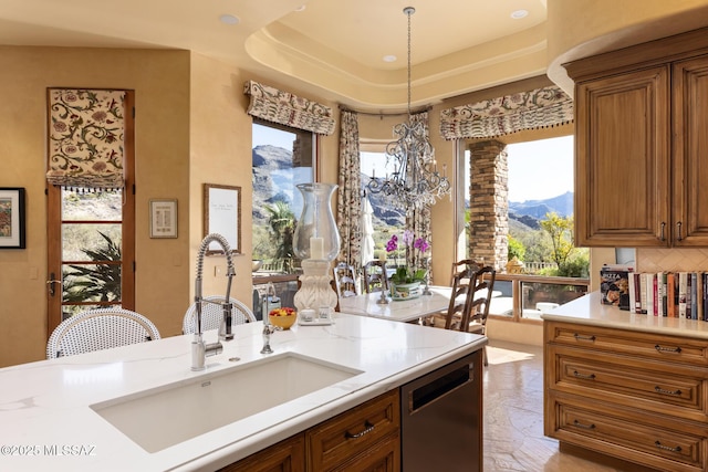 kitchen featuring a tray ceiling, a sink, a mountain view, dishwasher, and brown cabinets