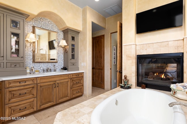 bathroom with vanity, tile patterned floors, visible vents, a tiled fireplace, and a bath